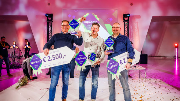 Drie lachende winnaars Topcoach 2024 op podium met award en geldprijs in de hand.