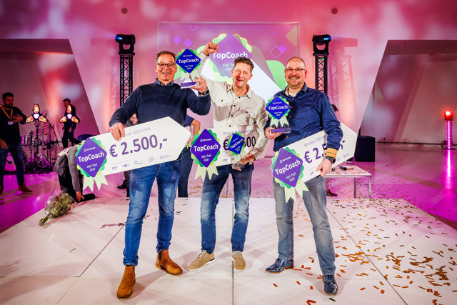 Drie lachende winnaars Topcoach 2024 op podium met award en geldprijs in de hand.