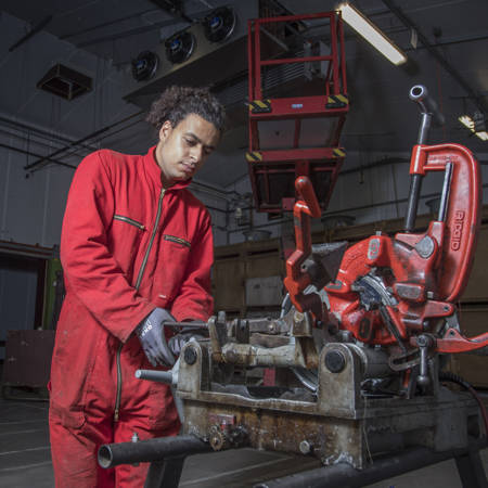 De Aftrap - Medewerker in rode overall aan het werk met technische installatie