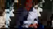 Roel Van Stokkum Eigenaar Elektrobedrijf Verweij in een wit overhemd en spijkerbroek zit op een stoel in een schemerige gang en lacht naar de camera.