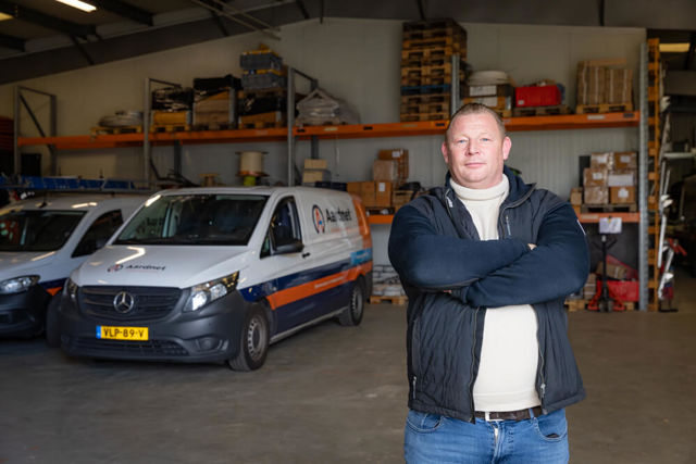 Robbert Jan De Haan, eigenaar Ardnet staat met z'n armen over elkaar voor twee busjes in een loods met allerlei machines en voorraad.