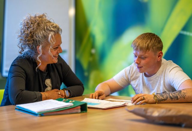 Lachende vrouwelijke praktijkopleider en jonge leerling van Installatiebedrijf De Haan in gesprek aan tafel