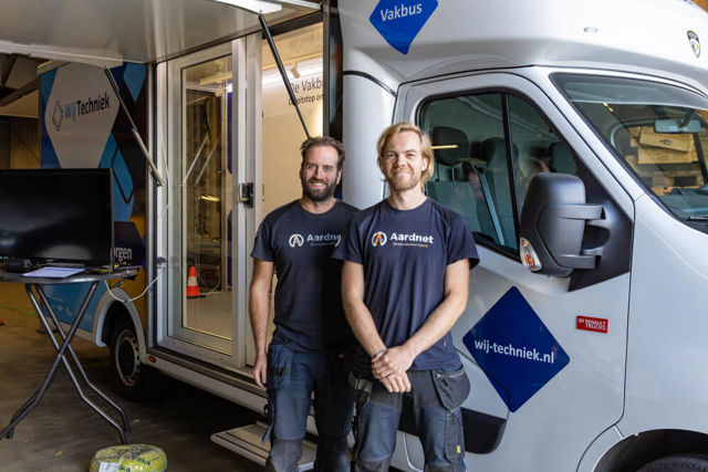 Twee monteurs van Aardnet staan voor een witte vakbus met Wij Techniek logo.