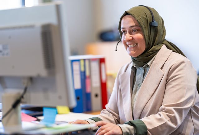 Kantoormedewerker Installatiebedrijf De Haan met headset lachend achter haar bureau en beeldscherm