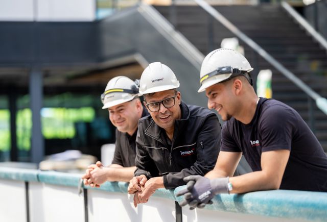 Sanjay Bhoendie (voormalig TopCoach van het Jaar) met twee studenten leunen nonchalant over reling bij een bouwplaats.